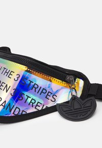 Černá ledvinka s holografickou kapsou na zip s textem. Součástí je černý gumový klíčenka s logem. Text kontrastuje s odrazivým povrchem.