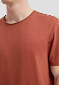 Roestkleurig t-shirt met een gladde, lichte textuur, voorzien van een ronde halslijn en korte mouwen. Subtiele gemêleerde patroon zichtbaar.