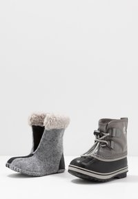 Um par de botas de inverno lado a lado: bota de feltro à esquerda com punho de lã, bota à direita em borracha e tecido impermeável com atacadores e sola com ranhuras.