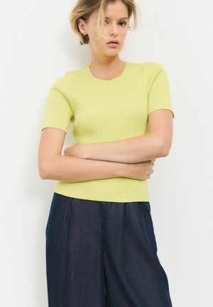 Ribbede kortærmede top i lys grøn; tætsiddende design. Parret med løse, mørke denimbukser. Glat tekstur, minimal detaljering.