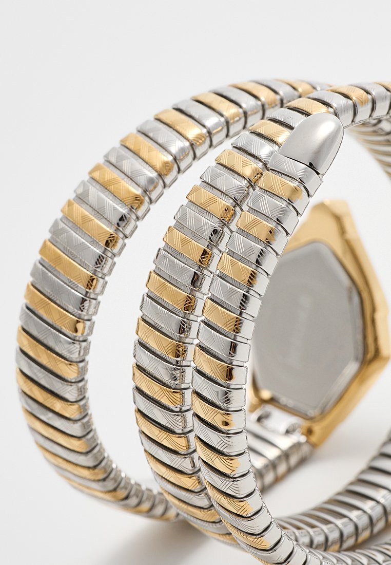 Reloj metálico con un diseño de dos tonos con acentos en plata y oro. La pulsera consiste en eslabones segmentados con un patrón. Caja hexagonal con un dorso liso.