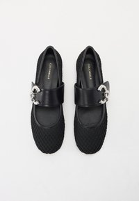Zapatos planos negros hechos de malla y cuero, con puntera redonda, textura trenzada y una tira ancha con un detalle de hebilla metálica.