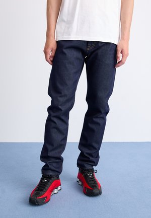 Dark blue denim jeans with a straight cut, paired with red and black athletic shoes featuring a thick sole. Simple white t-shirt.