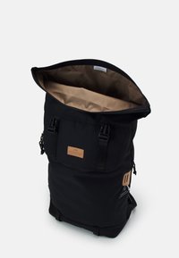 Černý batoh s rolovacím horním uzávěrem. Má světle hnědou vnitřní část, nastavitelné popruhy a koženou nášivku s logem. Pevná látka a minimalistický design.