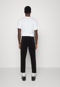 Svarta kordbyxor med rak klippning, bakfickor, kombinerat med en vit t-shirt och svarta skor, sedd bakifrån.