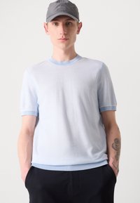 Pullover a maniche corte di colore azzurro chiaro, con scollo rotondo, bordi a costine in contrasto e una finitura texturizzata. Modello che indossa pantaloni scuri.
