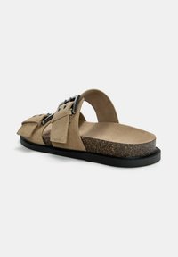 Beigefarbene Wildledersandalen mit zwei verstellbaren Riemen und einem strukturierten Fußbett. Sie verfügen über eine Kork-Zwischensohle und eine schwarze Gummisohle.