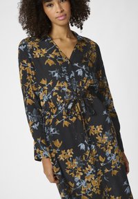 Robe noire à manches longues, avec un motif floral en or et bleu. Comprend une ceinture à nouer à la taille et des boutons sur le devant.