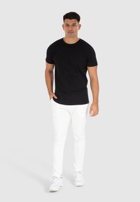 Zwarte katoenen t-shirt met korte mouwen, gecombineerd met witte slim-fit jeans en witte sneakers, met een eenvoudig en schoon ontwerp.