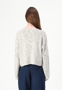 Jasnoszary krótki sweter z fakturowanym splotem, z okrągłym dekoltem i długimi rękawami, zestawiony z ciemnymi spodniami dżinsowymi.