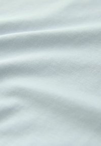 Glattes hellblaues Stoffmaterial mit sanften Falten, das eine feine Webstruktur und subtile Schatten durch das drapierte Material zeigt.