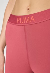 Puma-brändin vaaleanpunaiset legginsit, joissa on sileä pinta, leveä vyötärö ja minimitikkaukset. Lähellä otettu kuva kankaasta.