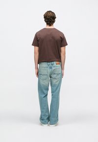 Καφέ βαμβακερό μπλουζάκι συνδυασμένο με ανοιχτό μπλε, ελαφρώς φθαρμένο τζιν παντελόνι. Το τζιν διαθέτει κλασικό σχεδιασμό με πέντε τσέπες.