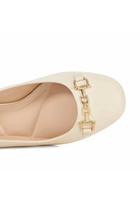 Beige ballerina met een ronde neus, bovenkant van glad patentenleer en een goudkleurige kettingdetail aan de voorkant.