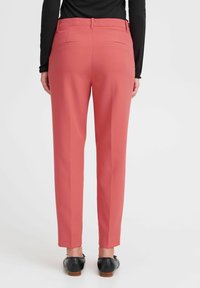 Roza hlače po meri s slim fit krojem, z zadnjimi žepi in gladko teksturo, v kombinaciji s črnimi čevlji. Ravnokotni kroj.