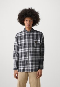 Black and white plaid shirt with a zip front, featuring a collar and a chest pocket with yellow logo. Soft fabric, long sleeves, relaxed fit.