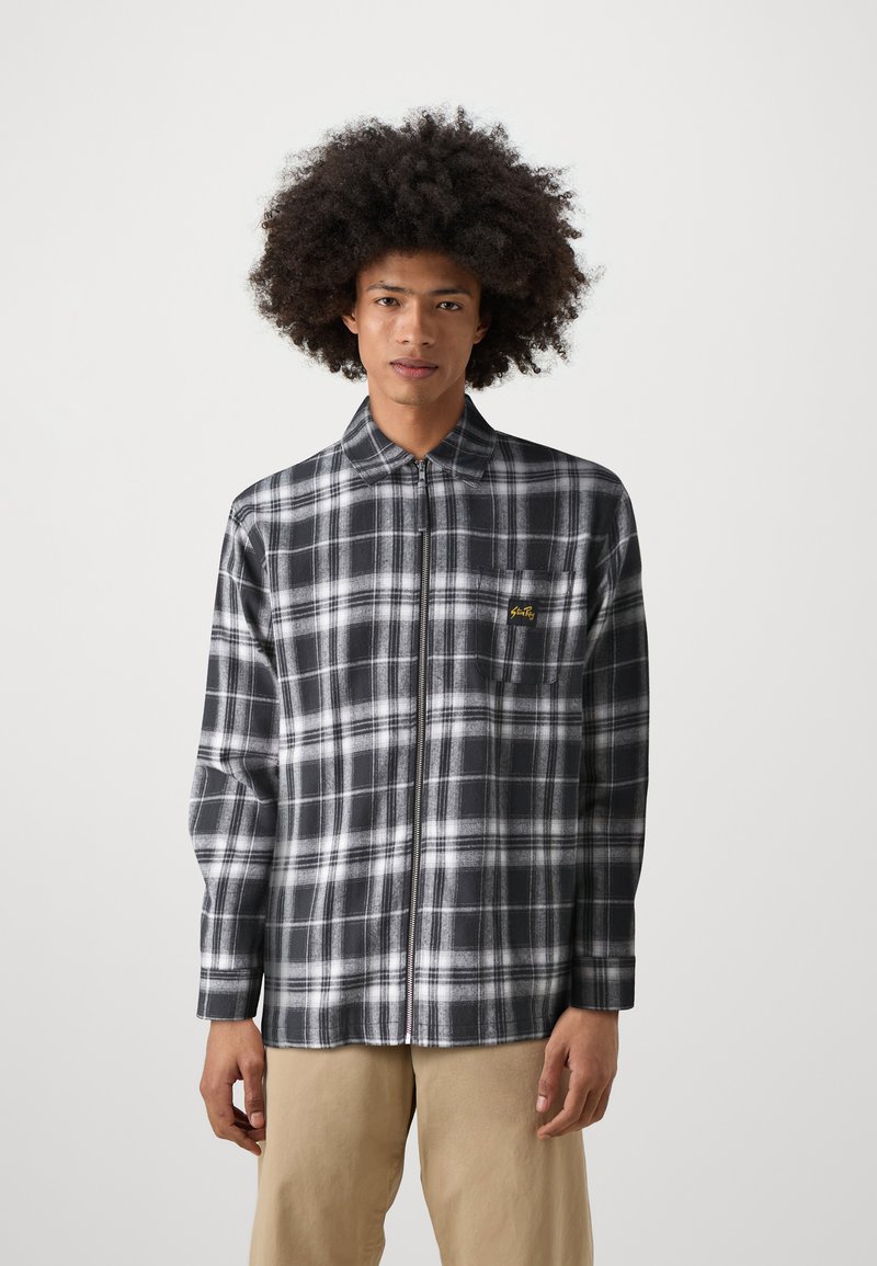 Black and white plaid shirt with a zip front, featuring a collar and a chest pocket with yellow logo. Soft fabric, long sleeves, relaxed fit.