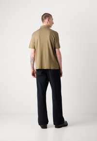 Polo à manches courtes de couleur olive avec un ourlet droit, porté avec un pantalon large bleu foncé et des chaussures noires, mettant en avant un design simple.