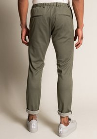 Olive green joggers with a tapered fit, elastic waistband, and two back zip pockets, paired with light-colored sneakers and cuffed hems.