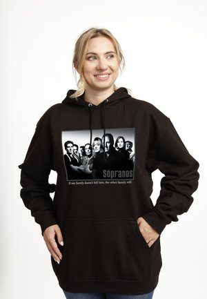 Kvinde iført sort hættetrøje med sort-hvid grafik af The Sopranos-castet og tekst med "If one family doesn't kill him, the other family will."