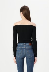 Sweater preto com nervuras, com decote ombro a ombro e mangas longas, combinado com jeans de ganga azul com um remendo de couro e bolsos traseiros costurados.