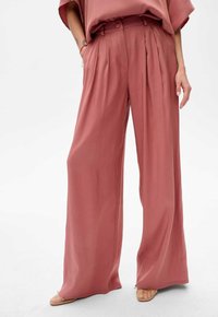 Spodnie o szerokich nogawkach w delikatnym odcieniu różu. Wykonane z gładkiego materiału z subtelnym połyskiem. Posiadają pliski oraz wysoki stan z szlufkami na pasek.