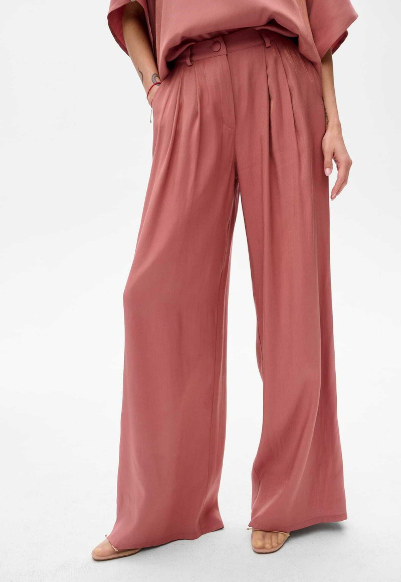 Spodnie o szerokich nogawkach w delikatnym odcieniu różu. Wykonane z gładkiego materiału z subtelnym połyskiem. Posiadają pliski oraz wysoki stan z szlufkami na pasek.