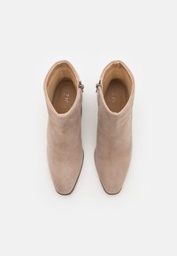 Stivaletti alla caviglia in suede beige con punta appuntita e dettagli con cerniera. Presentano una texture liscia e un design elegante e minimalista.