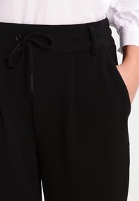 Zwarte textuurbroek met een trekkoord in de taille, zijzakken en een losse pasvorm, gecombineerd met een wit overhemd met knopen.