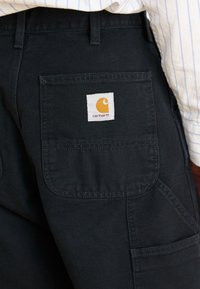 Black cargo pants made of durable fabric with multiple pockets. Features a white tag with an orange logo on the back pocket.