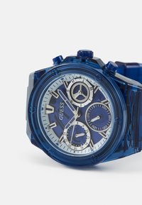Blauwe transparante kunststof horloge met een witte en blauwe wijzerplaat, drie subwijzers, zilveren accenten en prominente uurmarkeringen.