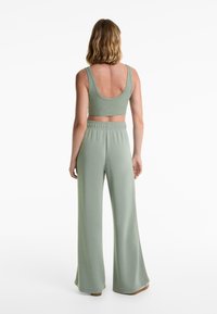 Rímský, svetlozelený crop top so širokými ramienkami, v kombinácii s rovnako farebnými, vysokými, voľne strihanými nohavicami a miernym rozšírením na leme.