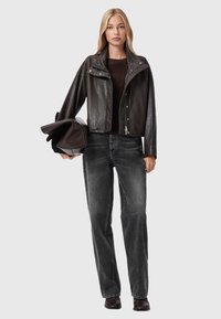 Melnas ādas īsa jaka ar sudraba rāvējslēdzēju detalizāciju, valkāta virs tumša džempera, kombinēta ar izbalējušām melnām taisnām biksēm.