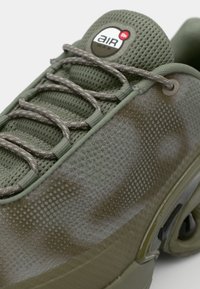 Olive green sneaker with mesh upper, circular perforations, and contrasting textured rubber sole. Features gray laces and logo on tongue.