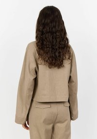 Beige kurzes Jackett mit glatter Textur, fallenden Schultern und Rückenpasse, kombiniert mit passender, hochtaillierter Hose.