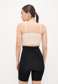 Beige stretchy crop top with thin straps paired with high-waisted black shapewear shorts, featuring a smooth texture and form-fitting design.