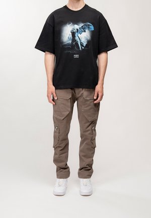 Sort t-shirt med korte ærmer med et grafisk print i blå og hvid. Kombineret med tan cargo-bukser med flere lommer og lynlåse. Hvide sneakers.