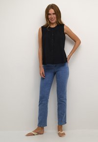 Canotta blu navy senza maniche con chiusura a bottoni, dettagli plissettati, abbinata a jeans dritti azzurri e sandali. Outfit semplice e casual.