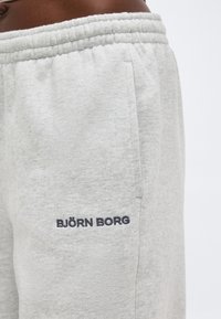 Κοντινό πλάνο ανοιχτό γκρι φόρμας με ελαστική μέση και κεντημένο λογότυπο "BJÖRN BORG" κοντά στην μπροστινή τσέπη.