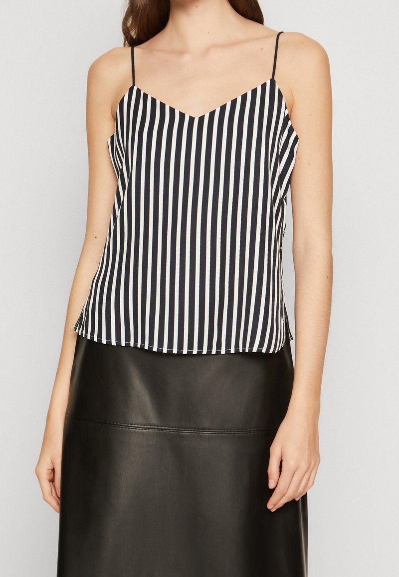Schwarz-weiße gestreifte ärmellose Bluse mit V-Ausschnitt und lockerer Passform, aus leichtem Stoff. Wird über einem schwarzen Lederrock getragen.