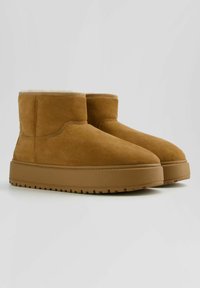 Bruna mockaskinnsankelkängor med en beige syntetpälsfoder och en tjock gummisula med ett strukturerat mönster.