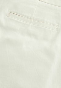 Tejido de algodón color beige claro con una textura suave, que presenta un bolsillo trasero rectangular con costuras en contraste.