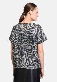 Fekete és ezüst flitteres felső zebra mintával, rövid ujjakkal, kulcslyuk hátrésszel és laza szabással. Sima textúra.