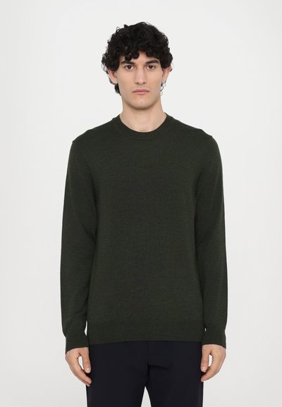 Pull en maille vert foncé avec un col rond et des manches longues, présentant une texture lisse et un design simple. Associe à un pantalon sombre.