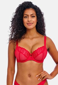 Sostén de encaje rojo transparente con borde en forma de ondas, soporte con varilla y un pequeño lazo central. Tirantes ajustables y acentos de patrón floral.
