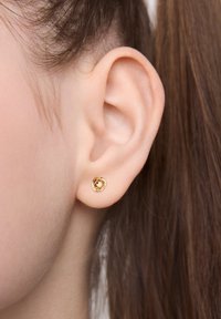 Złoty kolczyk w kształcie spirali na małżowinie usznej, o gładkiej fakturze i okrągłym kształcie. Zbliżenie podkreśla kształt i kolor kolczyka.