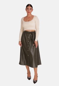 Top corto de canalé en color crema y falda midi de cuero sintético verde oliva con botones delanteros y cinturilla ajustable, combinado con zapatos negros de punta.