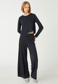 Top negro de manga larga y cropped con cuello redondo, combinado con pantalones holgados de pierna ancha en negro, hechos de un tejido suave y elástico.