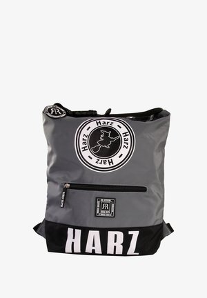 Grijze en zwarte rugzak met een glanzende afwerking. Voorzien van een voorzak met rits en een rond logo met tekst. Grote "HARZ" print aan de onderkant.