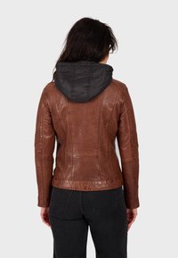 Giubbotto in pelle marrone con texture, dotato di cappuccio in nylon imbottito nero, design aderente e cuciture dettagliate, indossato su abbigliamento scuro.